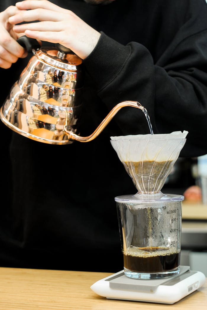 Close-up of hands pouring water in a pour-over coffee setup using a copper kettle.