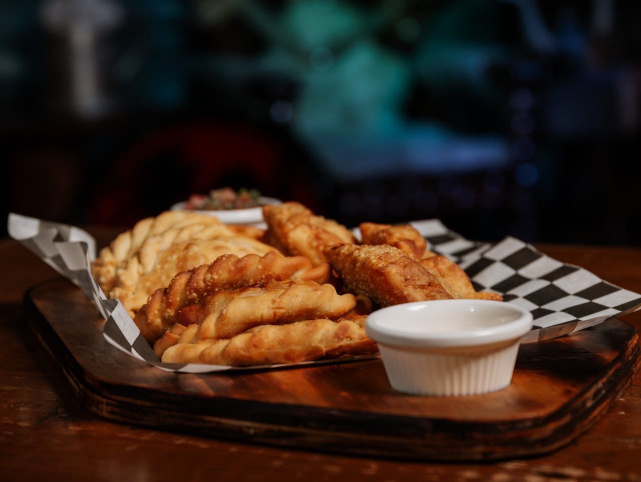 Tasty fried empanadas arranged on a wooden tray with a dipping sauce.