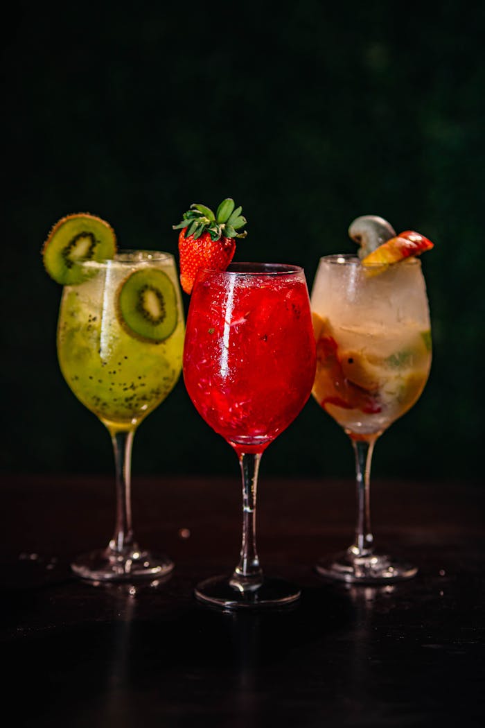 Three vibrant fruit cocktails with kiwi, strawberry, and peach garnishes in elegant glasses.