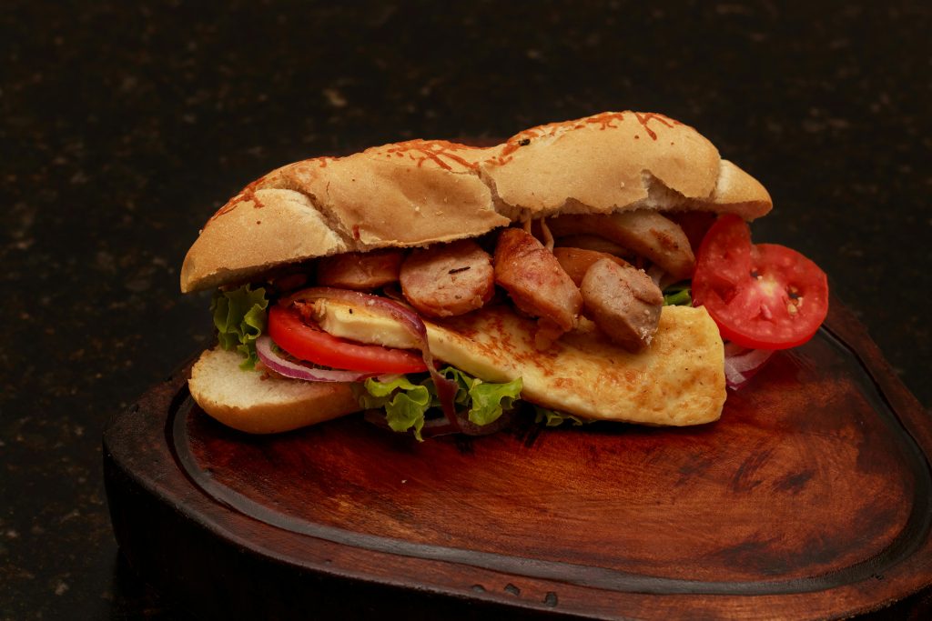 Tasty sandwich with fresh vegetables, meat, and cheese served on a wooden board.